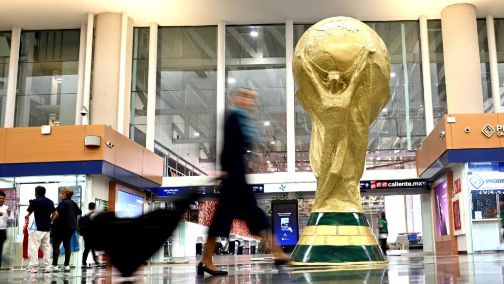 中国元素深度融入2026年美加墨世界杯_fororder_6月9日，在墨西哥首都墨西哥城的贝尼托·华雷斯国际机场的候机大厅，旅客从“大力神杯”模型旁走过