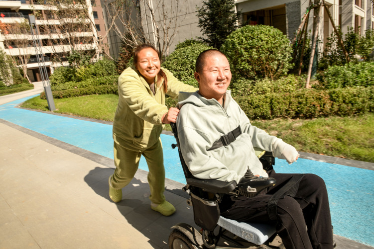 张春丽：把命运的“难”炼成日子的“暖”_fororder_张春丽推着丈夫散步，享受户外阳光沐浴。刘永兴 摄