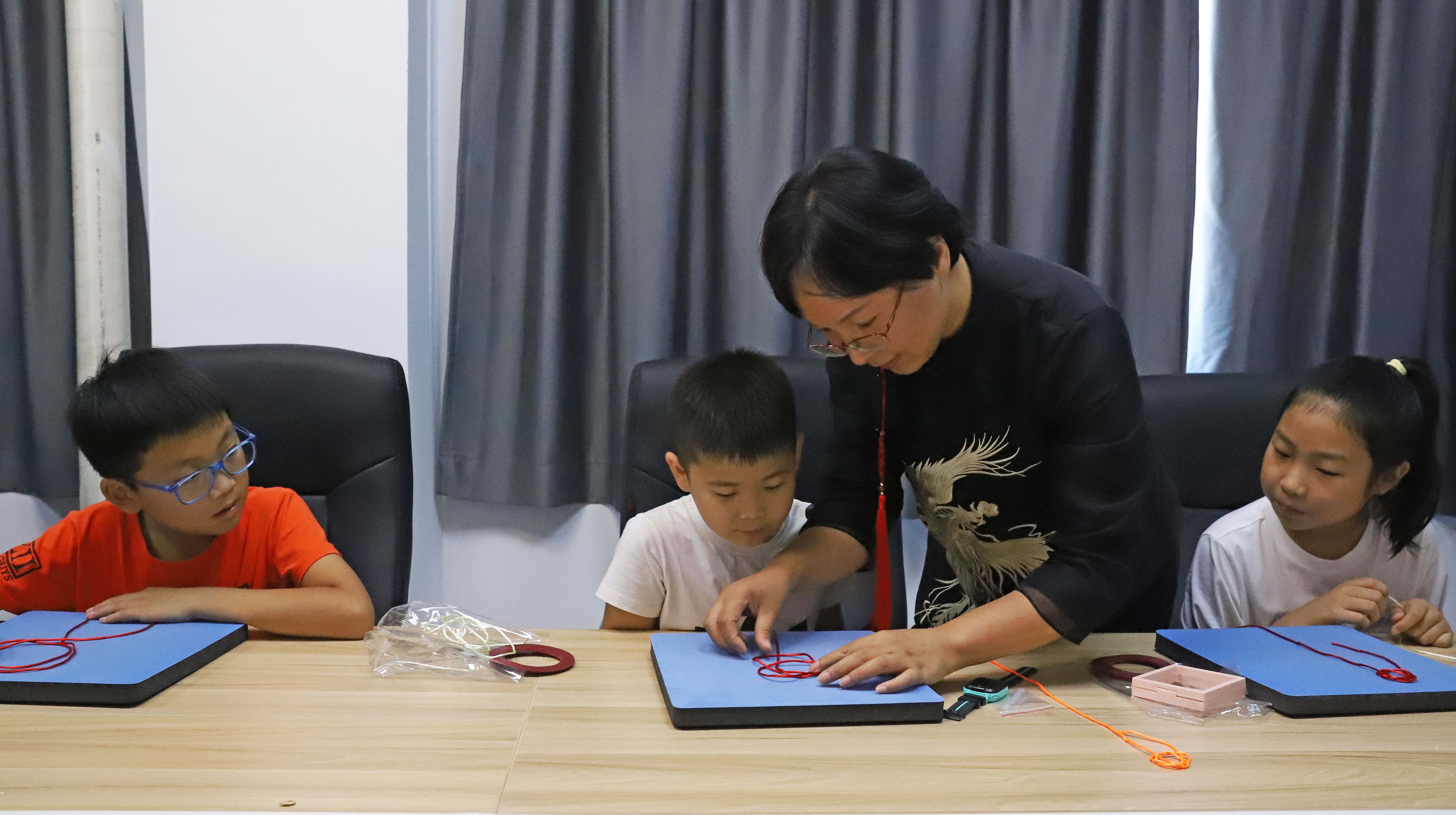 河北涿州：学生们假期生活增添“非遗色”_fororder_7月16日，涿州市非遗人传承人于长娟指导学生编织绳结。熊华明摄