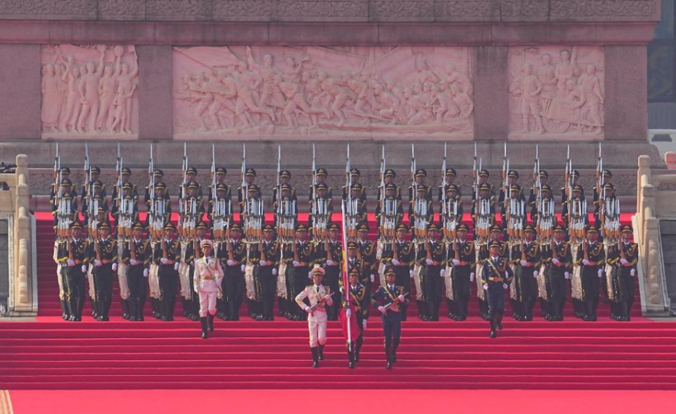 国旗护卫队官兵护卫着五星红旗，从人民英雄纪念碑行进至广场北侧升旗区